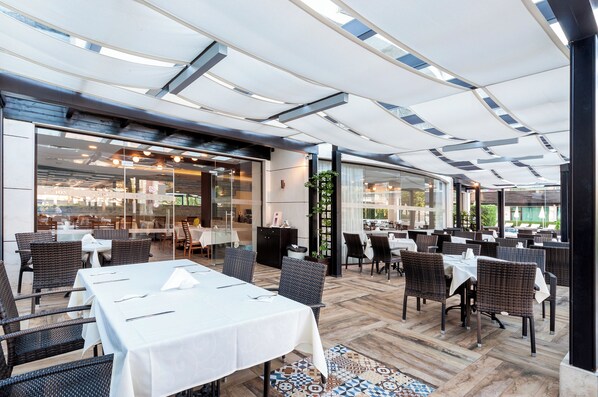 An indoor dining area with tables and chairs, large windows, and a ceiling with a unique design. - Hotel Lion Sunny Beach (Sunny Beach)