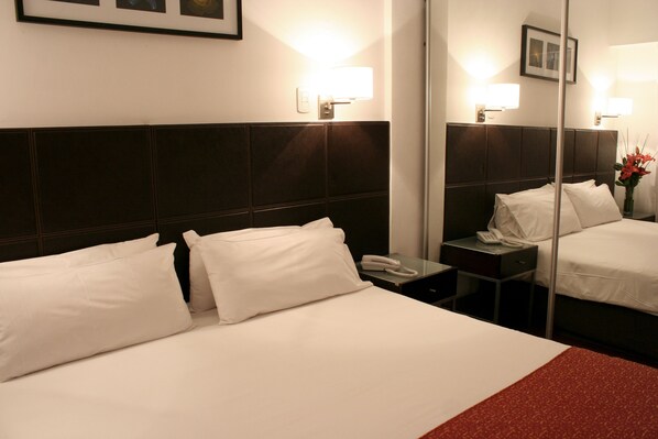 Une chambre d’hôtel avec un grand lit, une table de chevet avec un téléphone et un miroir qui reflète la pièce.