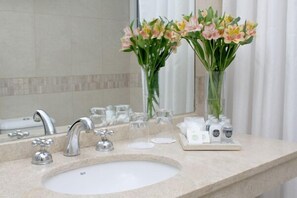 Une salle de bain avec un lavabo, deux robinets et deux vases de fleurs. On y trouve également des articles de toilette sur le comptoir.
