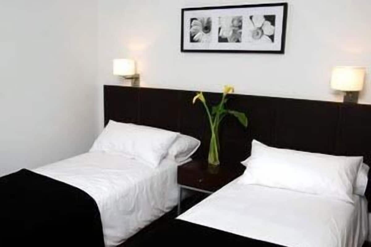 A hotel room with two single beds, a dark headboard, bedside lamps, and a framed picture on the wall.