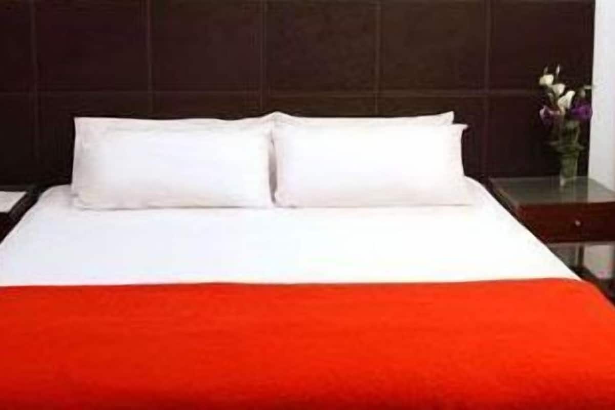 A hotel room with a bed, a nightstand, a phone, and a vase with flowers.