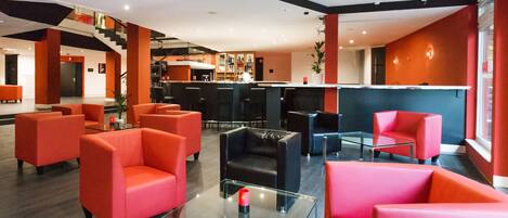 A modern lobby with red and black seating, a glass coffee table, and a bar area.