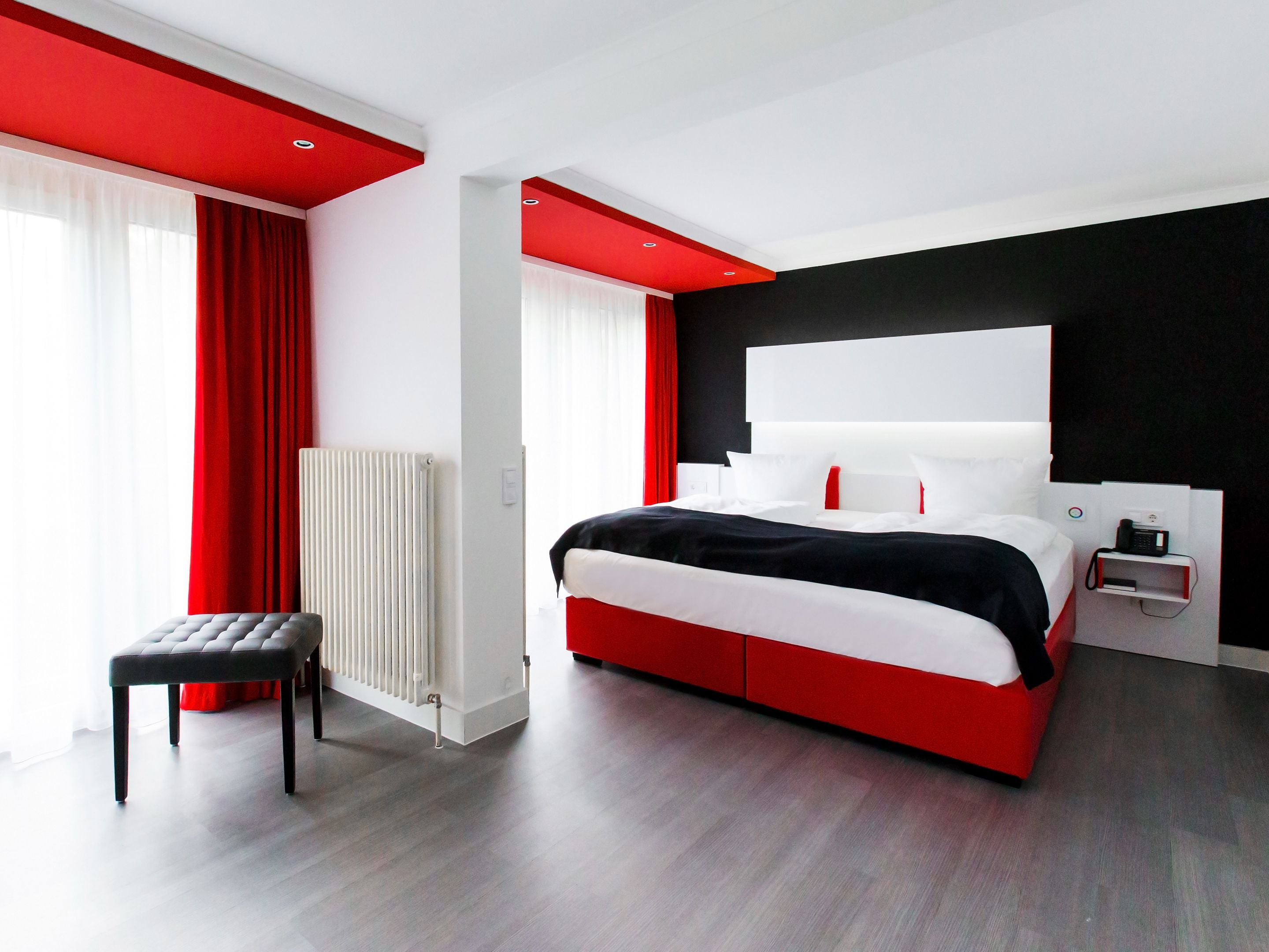 A modern hotel room with a large bed, a bedside table, a red and white color scheme, and a view of the city.