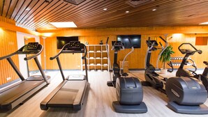 Un gimnasio con cintas de correr, elípticas y una pantalla de televisión en la pared.