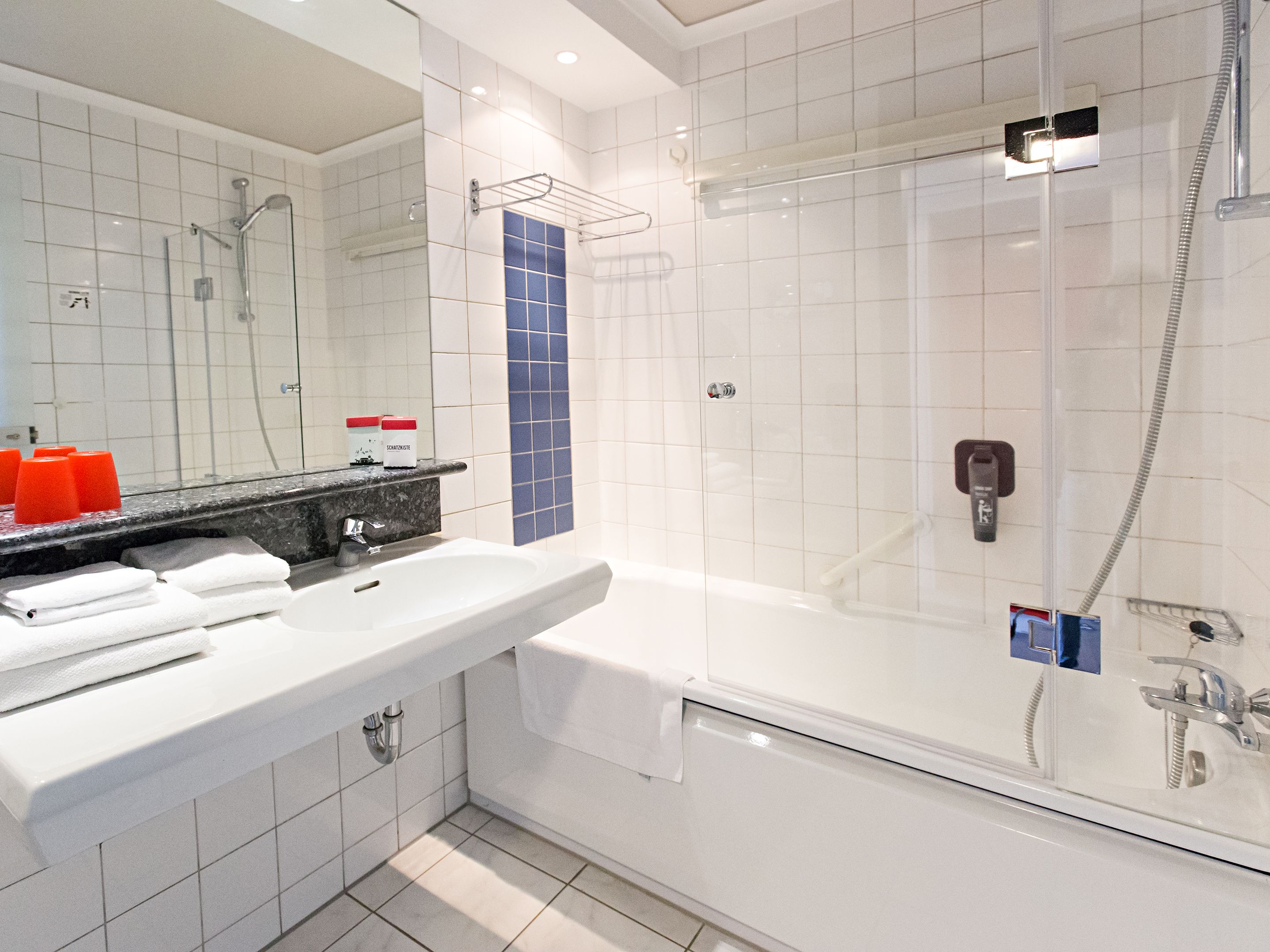 Un baño moderno con lavamanos blanco, espejo y cabina de ducha con paredes de vidrio.