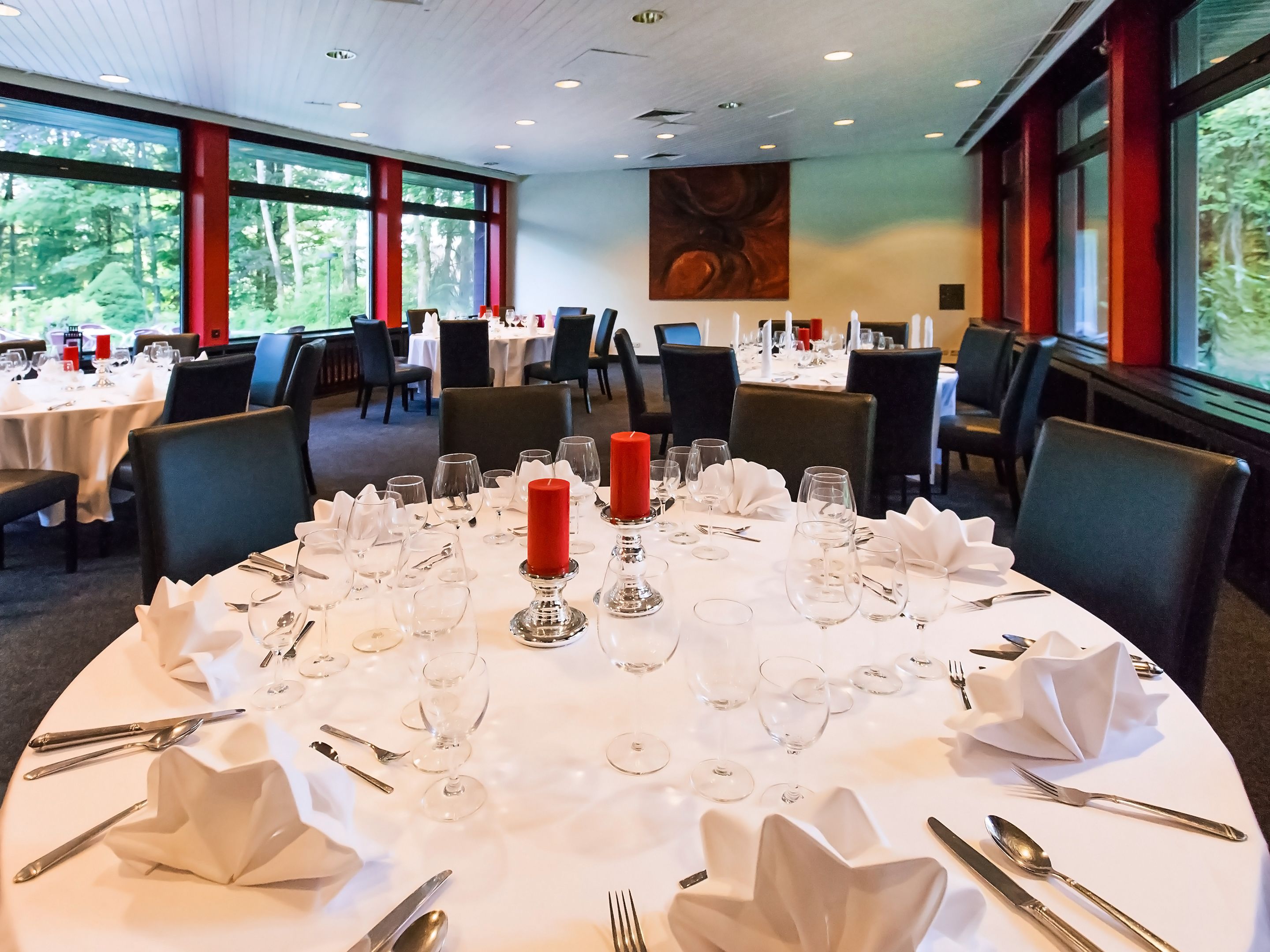 Ein Restaurant mit runden Tischen, gedeckt für das Essen, mit weißen Tischdecken, roten Kerzen und ordentlich platzierten Besteck.