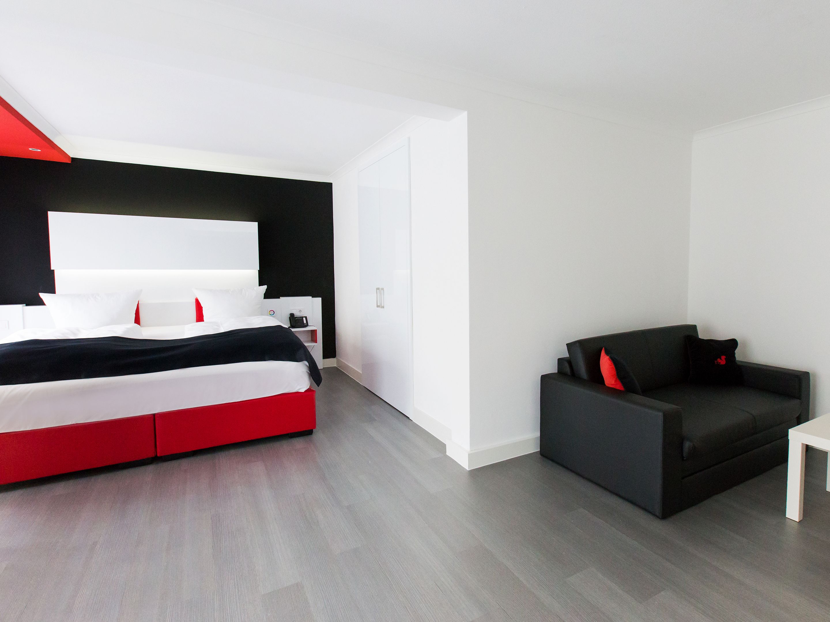 A modern hotel room with a large bed, a small sofa, and a desk.