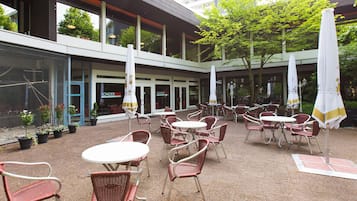 Eine Außenpatio-Terrasse mit Tischen, Stühlen, Sonnenschirmen und Blumentöpfen.