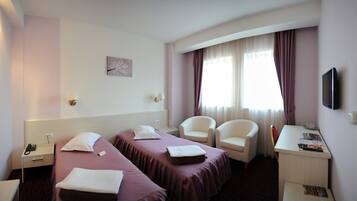 A hotel room with two beds, a desk, a chair, a TV, and a window with curtains.
