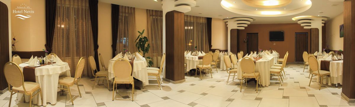 Un espace de restauration d’hôtel avec des tables rondes, des chaises et une grande plante.
