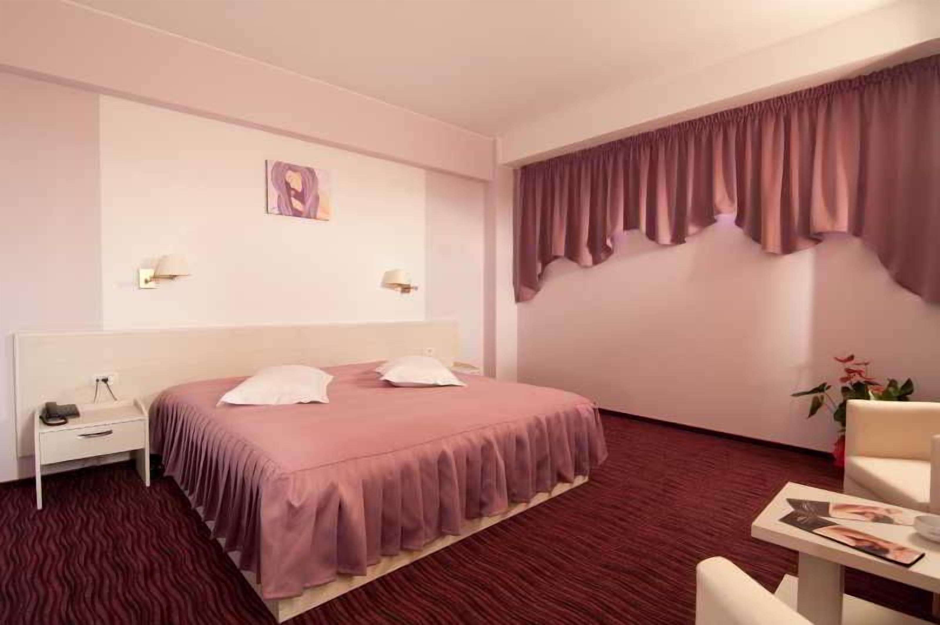 Habitación de hotel con cama, mesita de noche, lámpara y vistas al exterior.