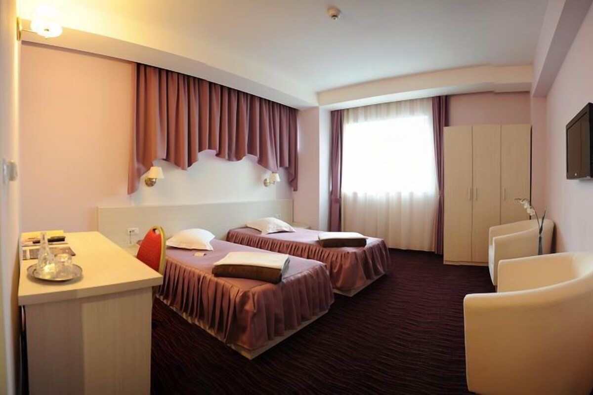 Habitación de hotel con dos camas, un escritorio, una silla y un televisor.
