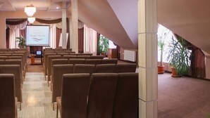 Une salle de conférence avec des rangées de chaises marron, un écran de projection affichant le texte « Hôtel Nevis Wellness & SPA », et un lustre.