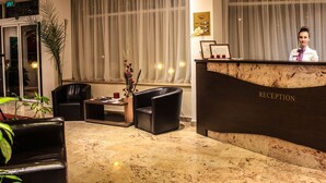 Un mostrador de recepción de hotel con encimera de mármol, sillones de cuero y plantas en macetas.