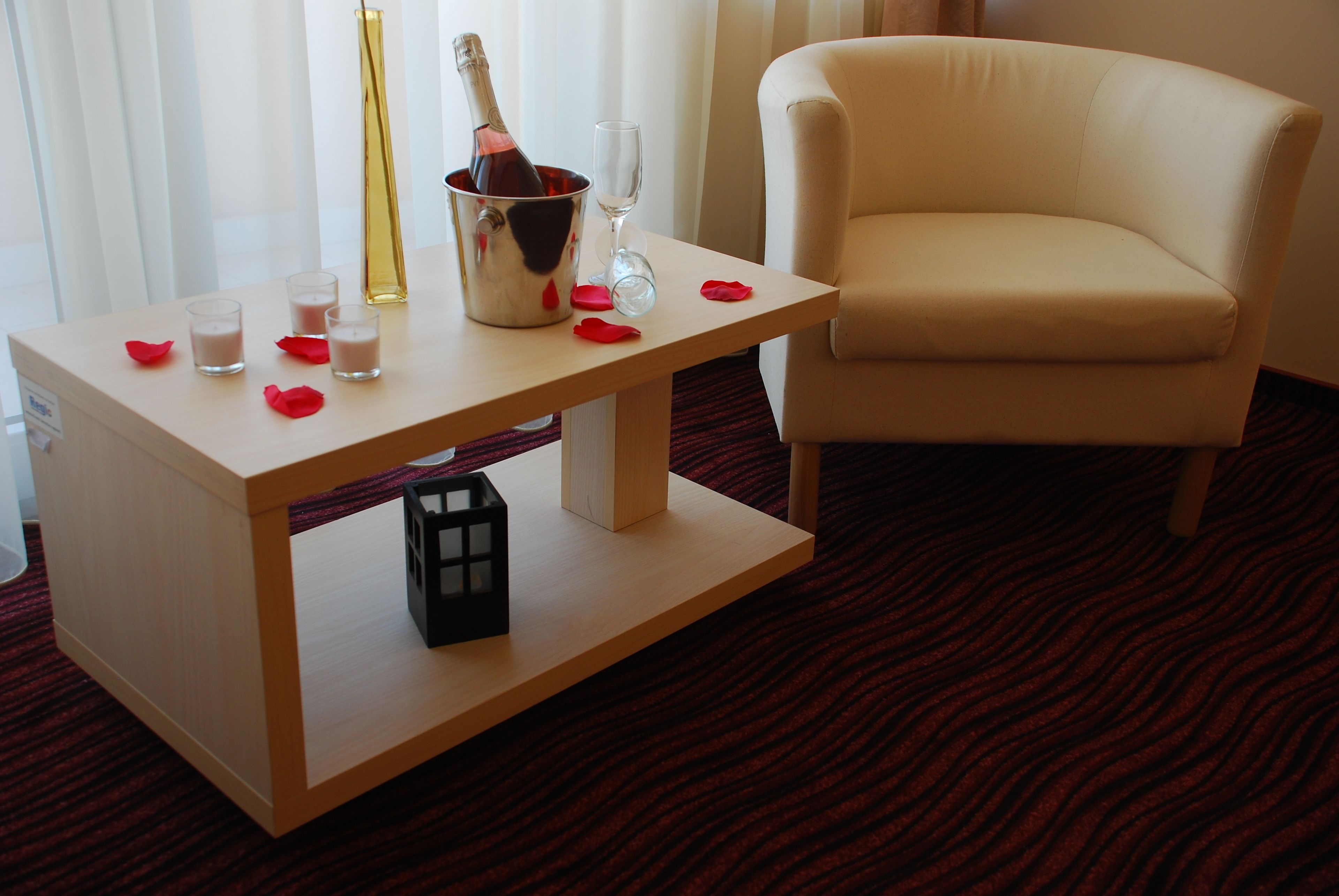 A hotel room with a wooden table, a bottle of champagne, and a glass.