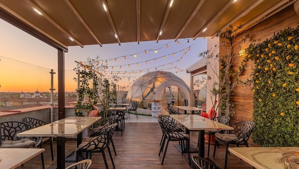An outdoor dining area with tables and chairs, a greenhouse structure, and a view of the cityscape.
