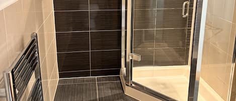 A modern shower room with dark tiles, a glass door, and a metal handle.