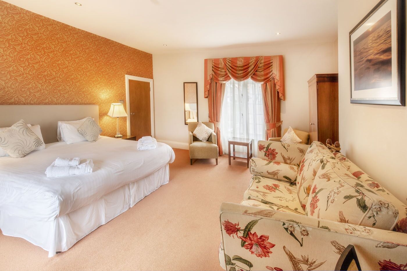 A hotel room with a large bed, a sofa, a chair, and a desk.