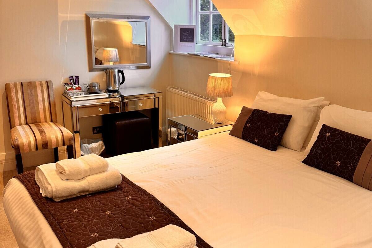 A hotel room with a large bed, a desk with a mirror, a chair, and a window with a view of trees.