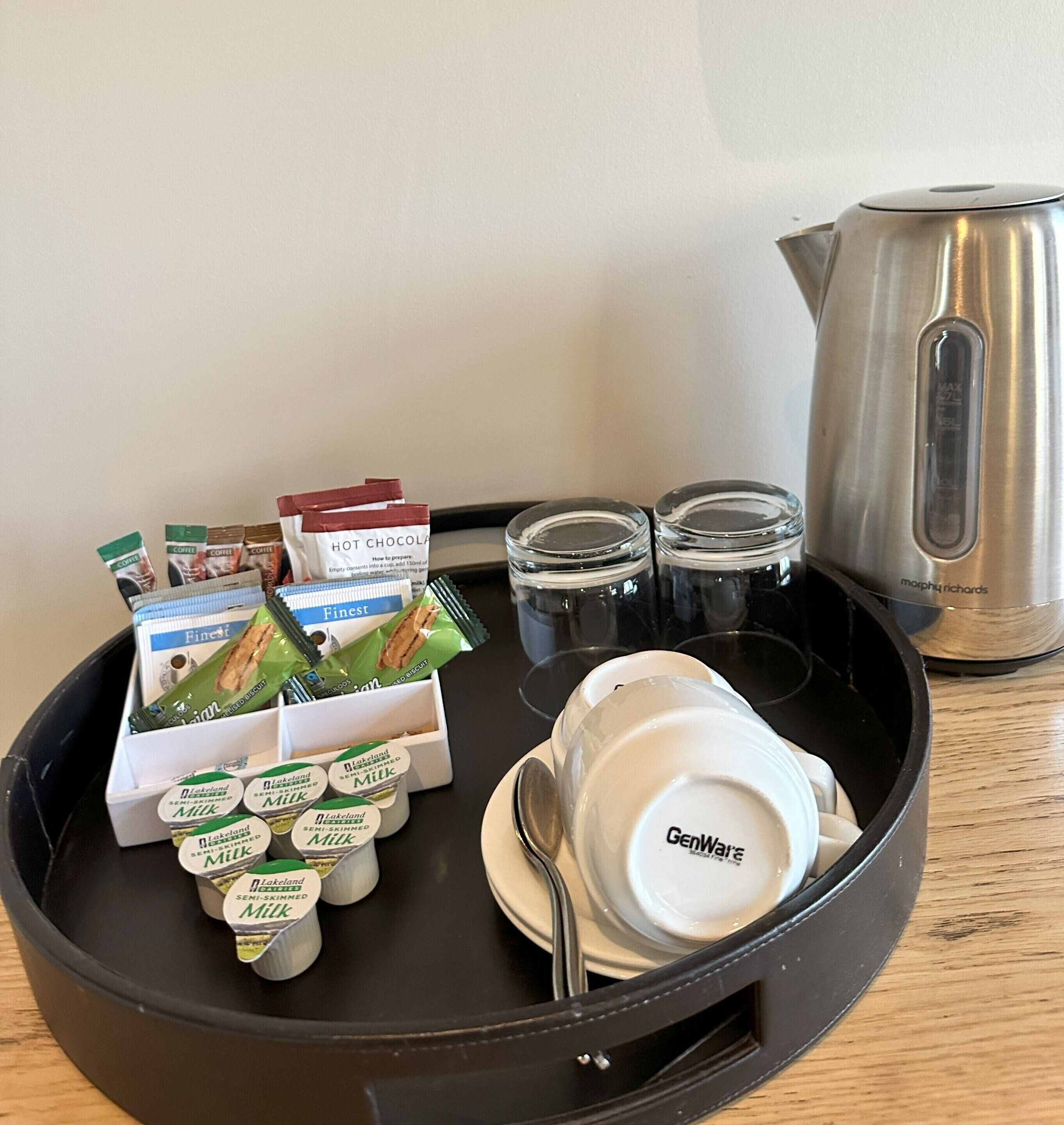 Un plateau avec des sachets de café, des briques de lait, une tasse et une bouilloire.