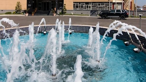 A hotel with a swimming pool and fountains, featuring a modern architectural design with multiple balconies and flags.