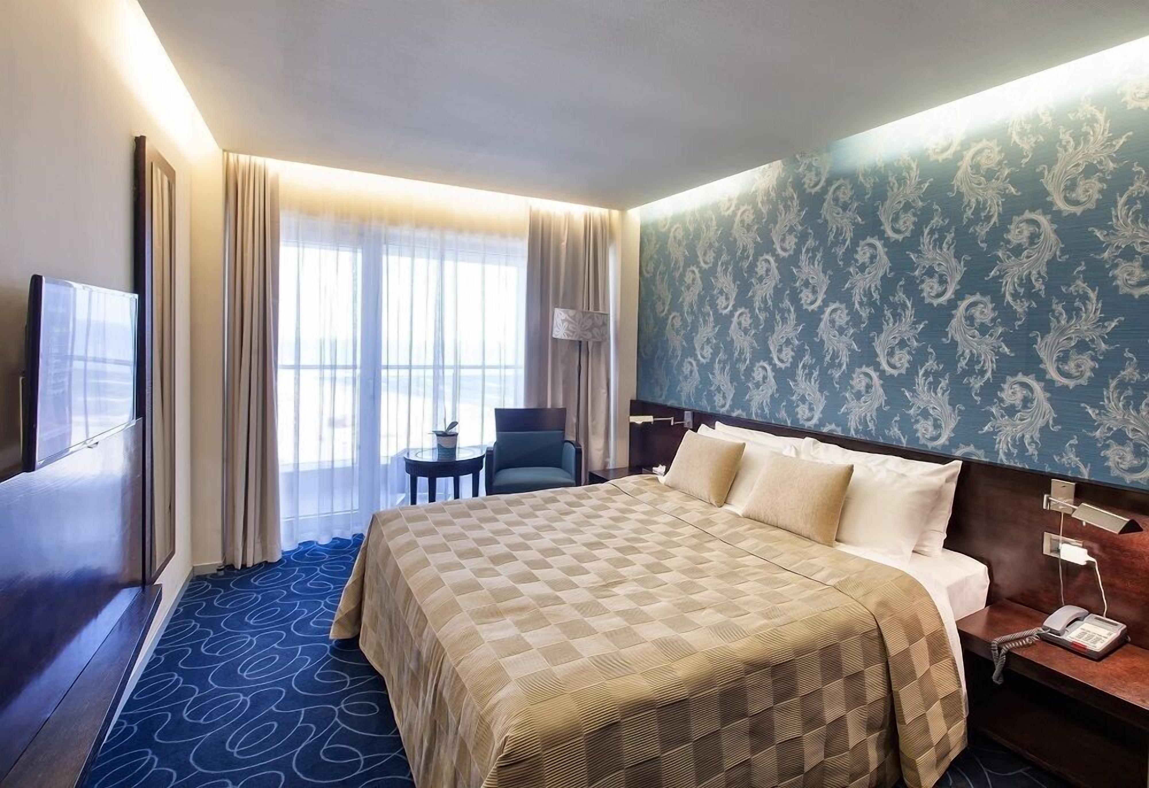 A hotel room with a large bed, a desk, a chair, a TV, and a window with curtains.