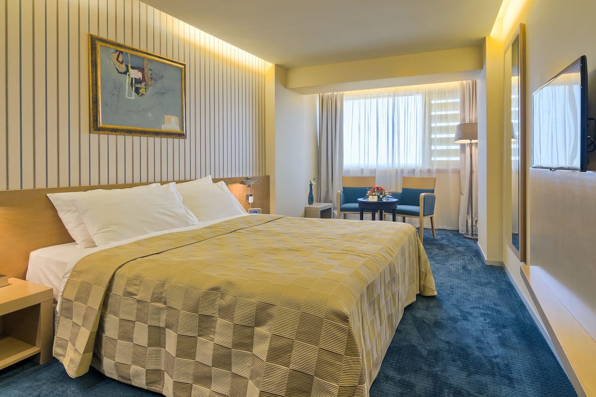 A hotel room with a large bed, a desk, a chair, and a TV.