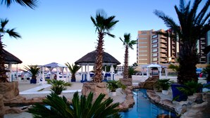 A pool area with palm trees, lounge chairs, and umbrellas.
