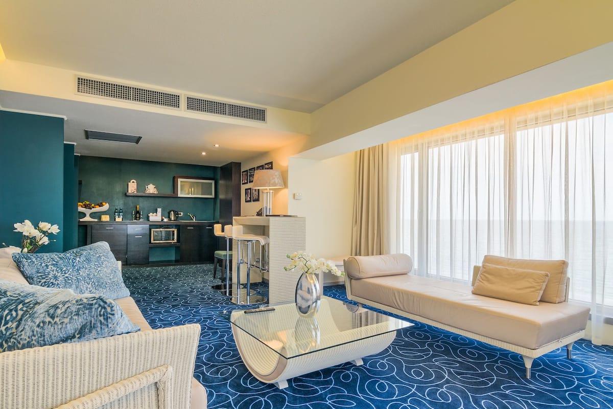 A hotel room with a living area, kitchenette, and a large window with curtains.