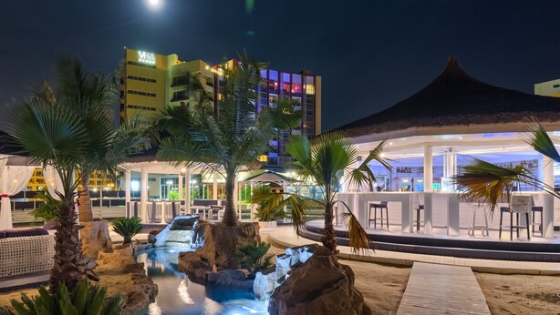 A nighttime resort with a pool, palm trees, and a bar area.