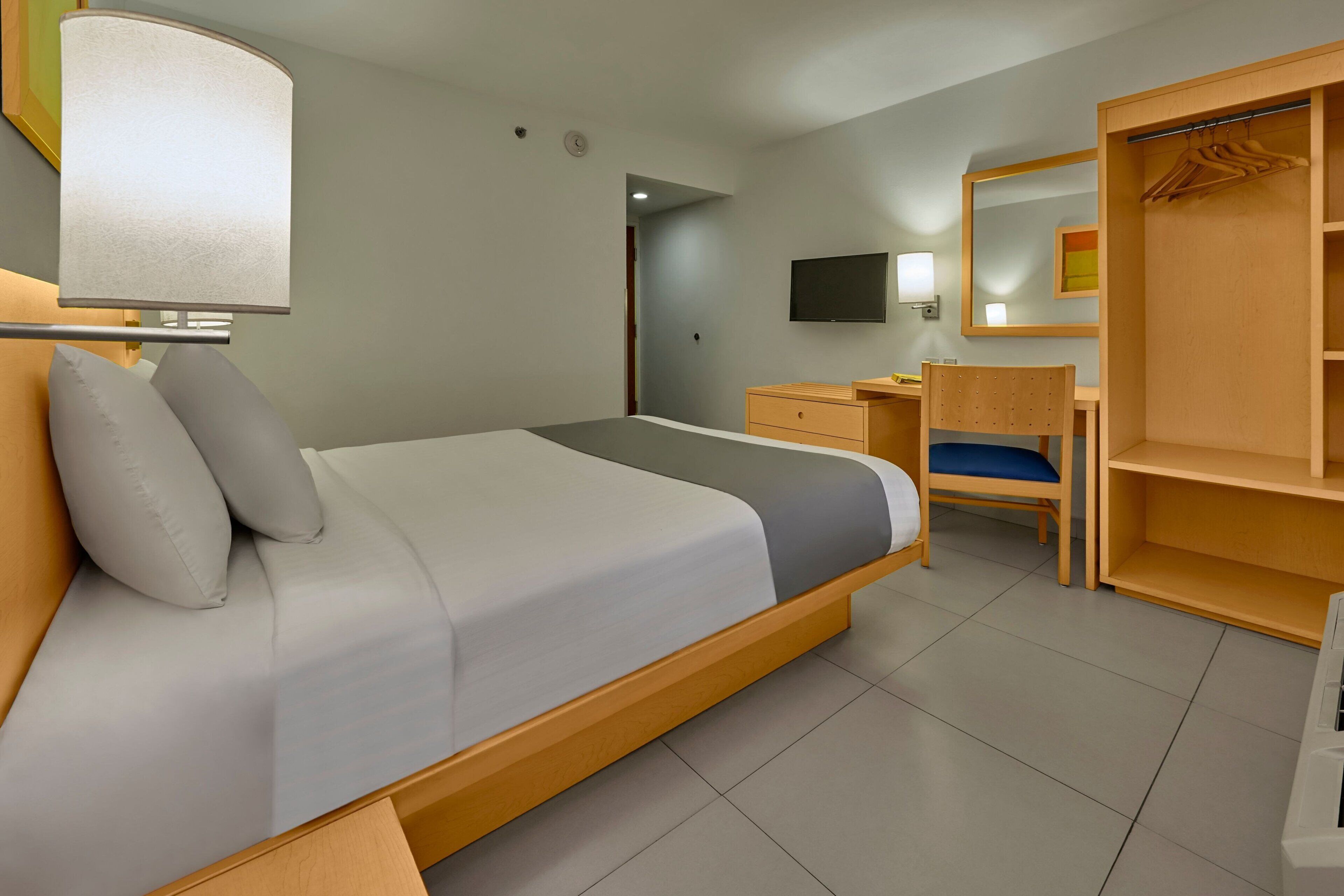 Habitación de hotel con cama, escritorio, silla, armario y televisor.