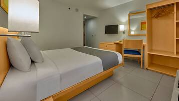 Habitación de hotel con cama, escritorio, silla, armario y televisor.