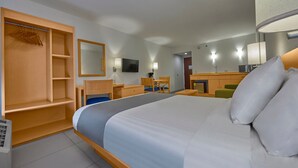 Habitación de hotel con una cama grande, un armario de madera, un escritorio, una silla y un televisor.