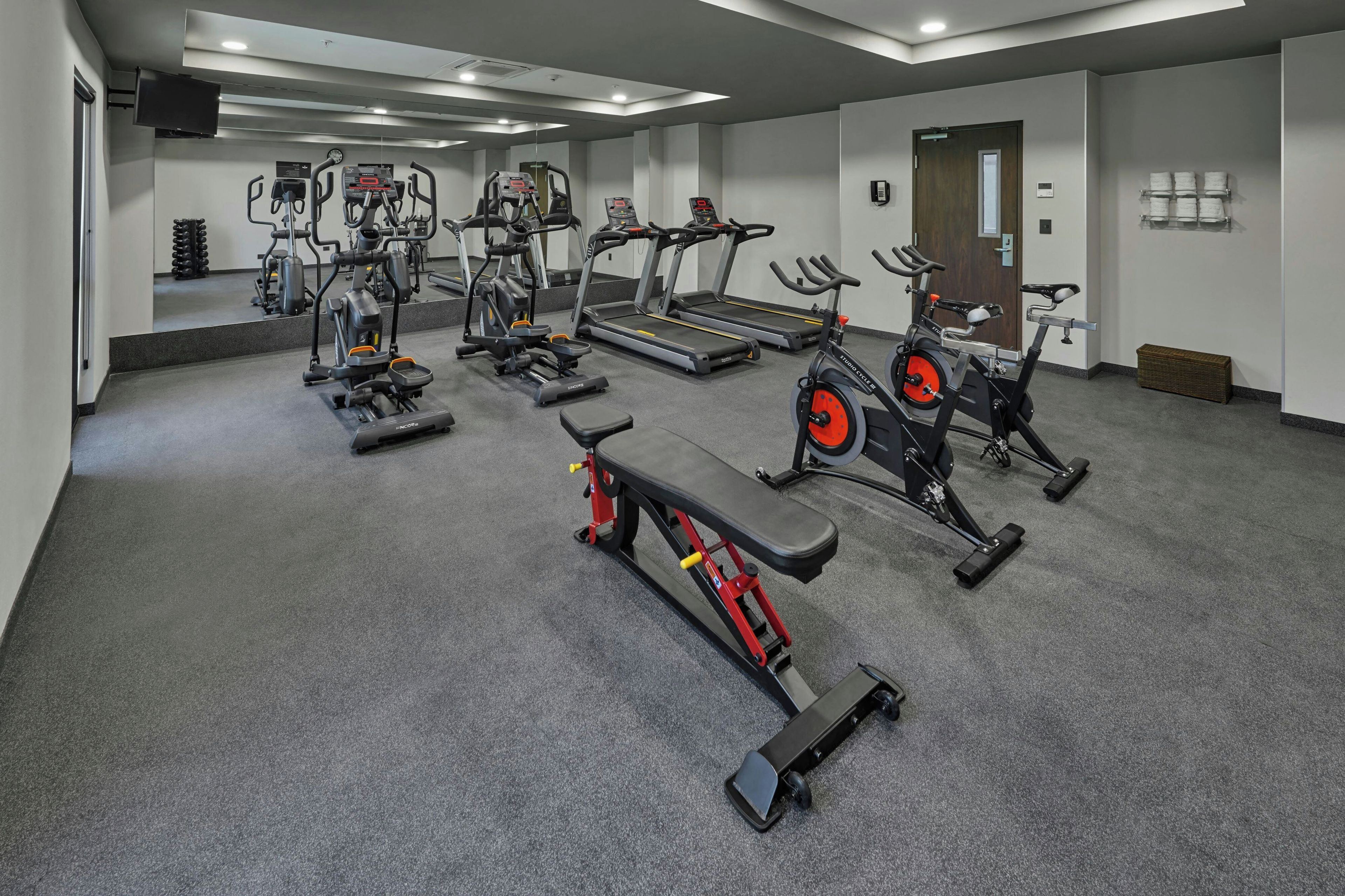 Un gimnasio con diversos equipos de ejercicio, incluyendo cintas de correr, bicicletas estáticas y una banca.