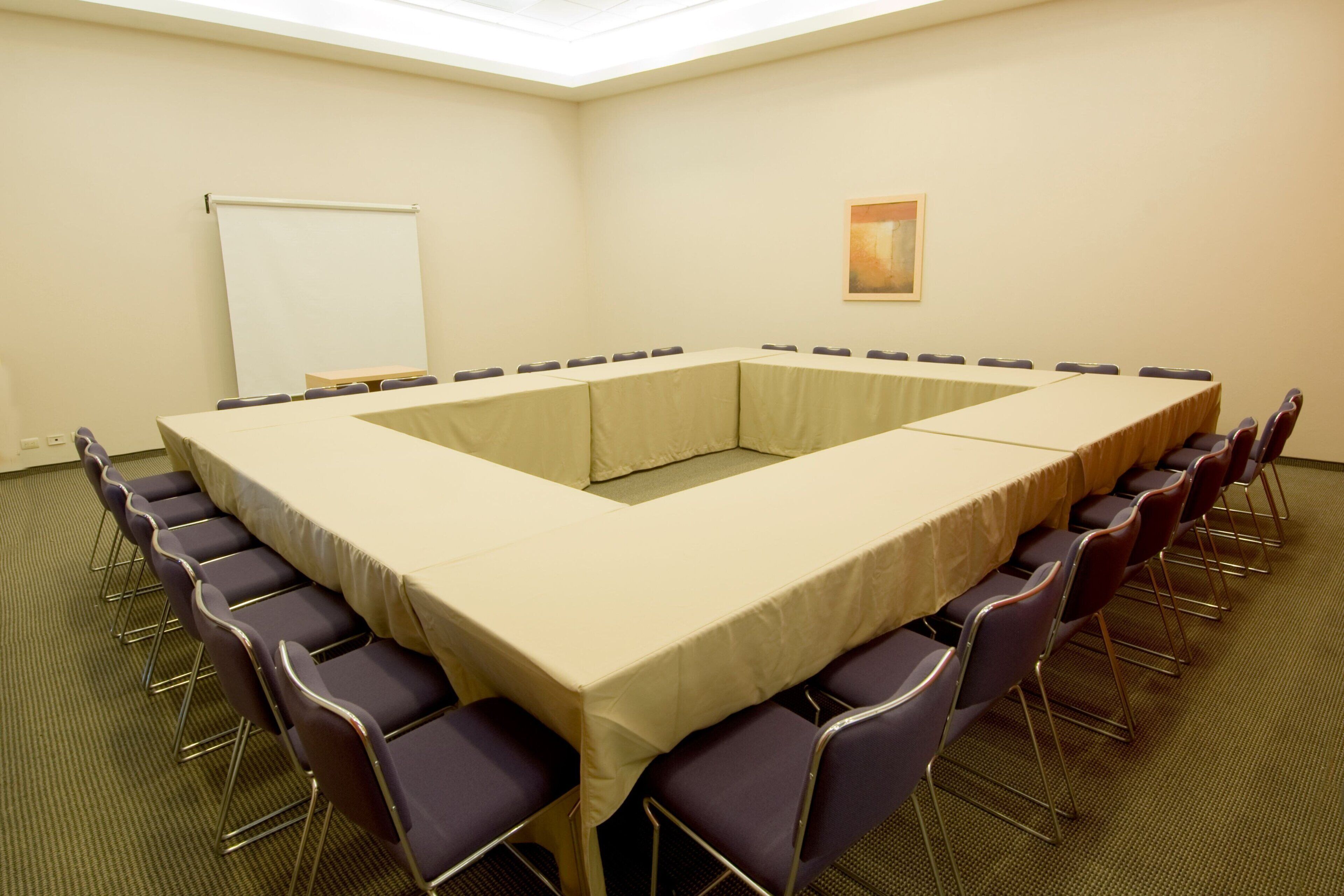 Ein Konferenzraum mit einem langen Tisch, Stühlen, einer Tafel und einem Bild an der Wand.