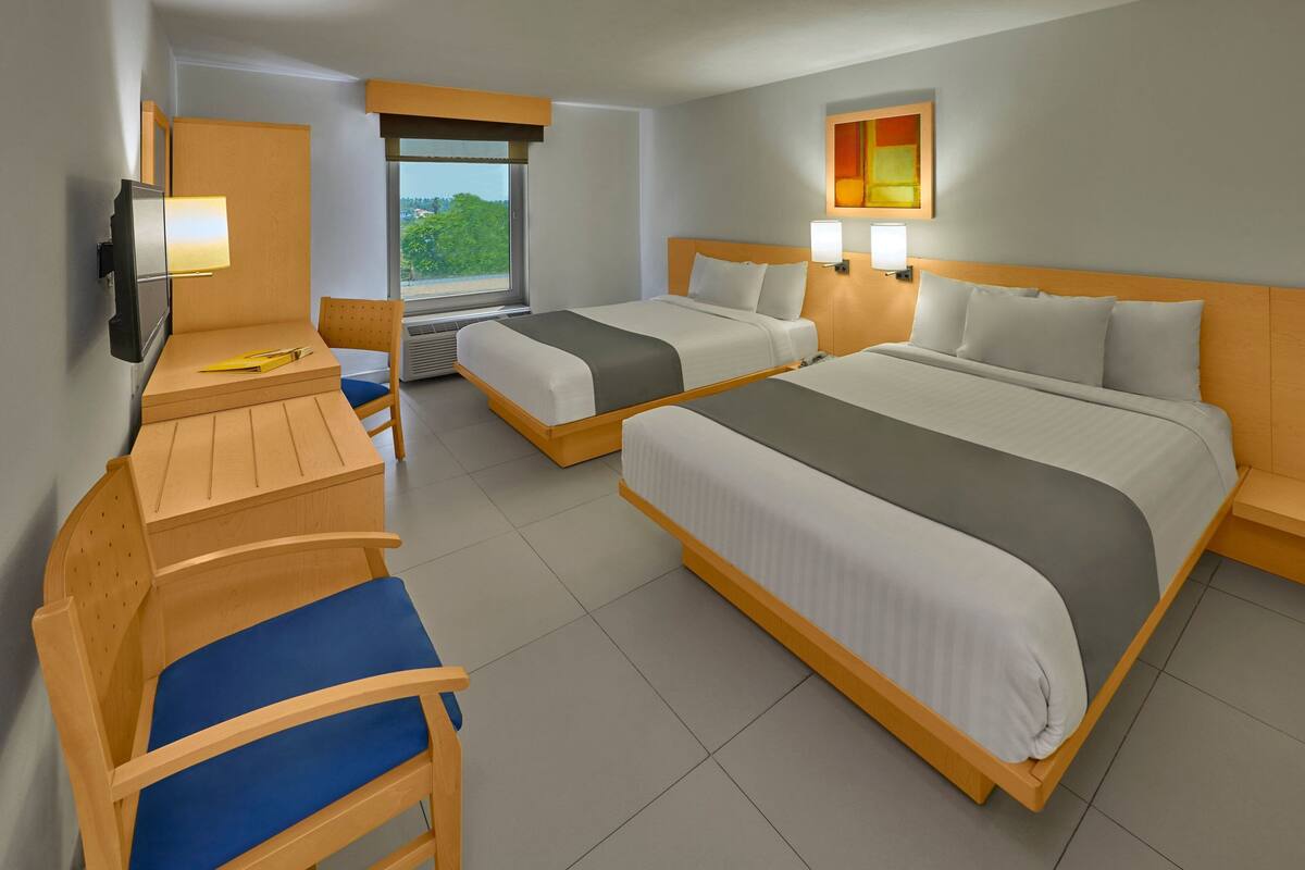 A hotel room with two beds, a desk, a chair, and a TV.