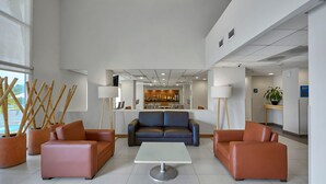 Un vestíbulo moderno con sofás de cuero, una mesa central y plantas de bambú en macetas.