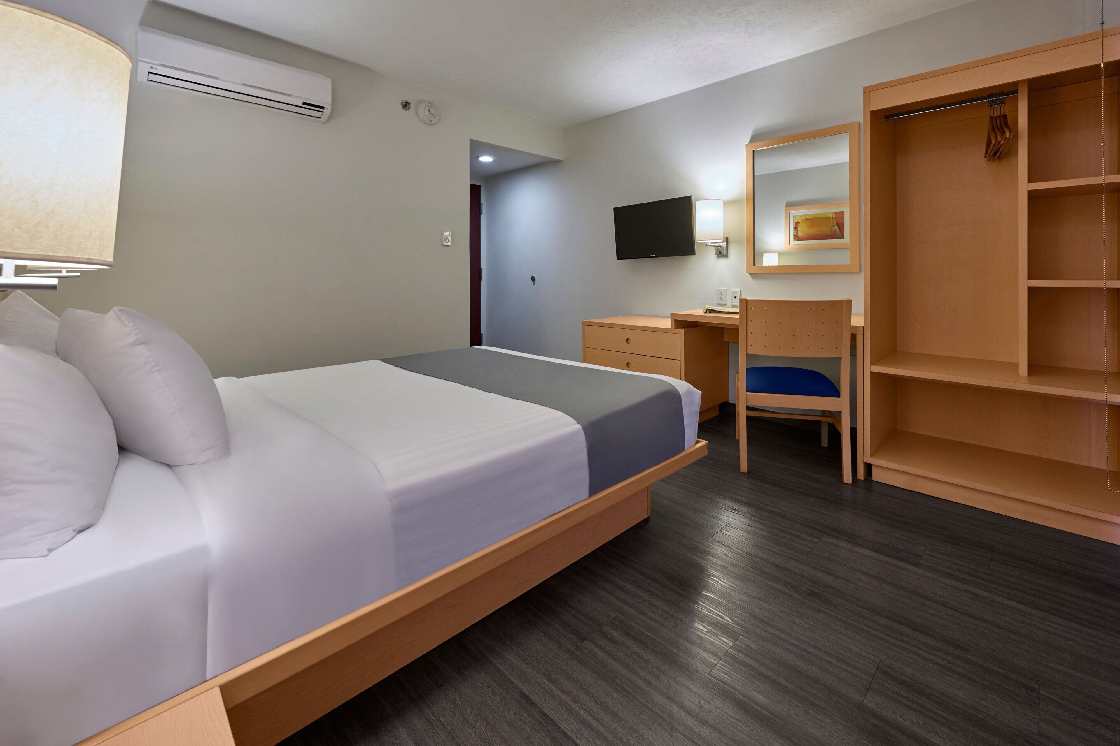 A hotel room with a bed, a desk, a chair, a wardrobe, and a TV mounted on the wall.