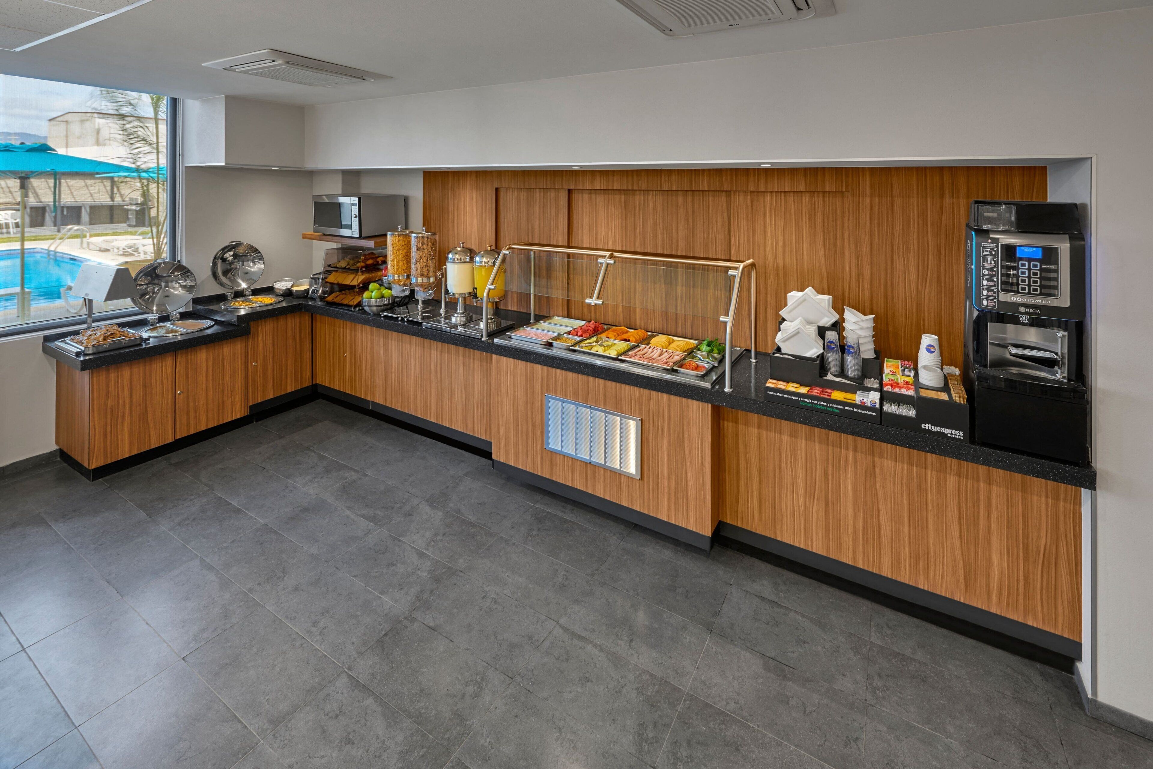 A buffet area with a variety of food options, a beverage dispenser, and a view of the pool outside.