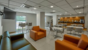 Un comedor moderno con asientos color naranja y marrón, un televisor de pantalla plana y una encimera de cocina con cafetera.