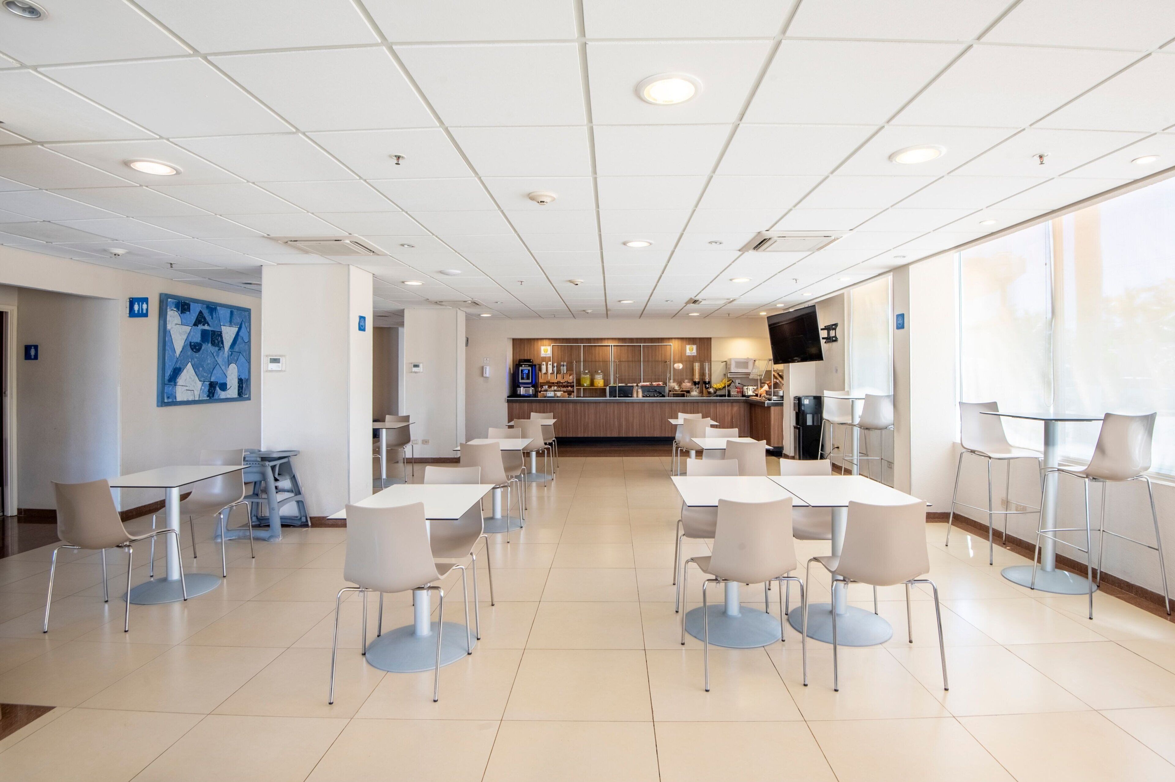 A spacious indoor area with multiple tables and chairs, a counter with various items, and a large window providing natural light.