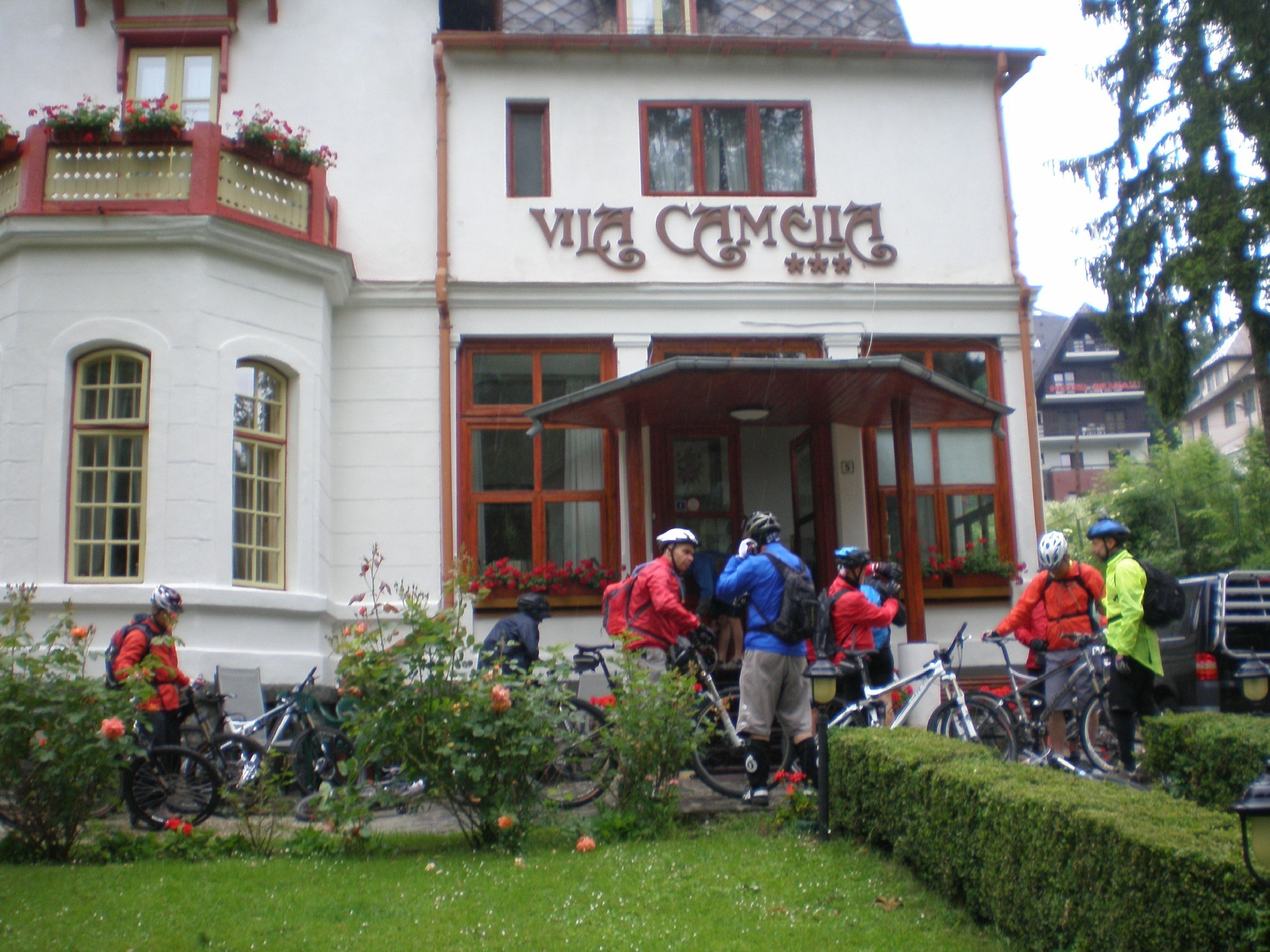 A building with a sign that reads "Vila Camela" and a group of people with bicycles in front.