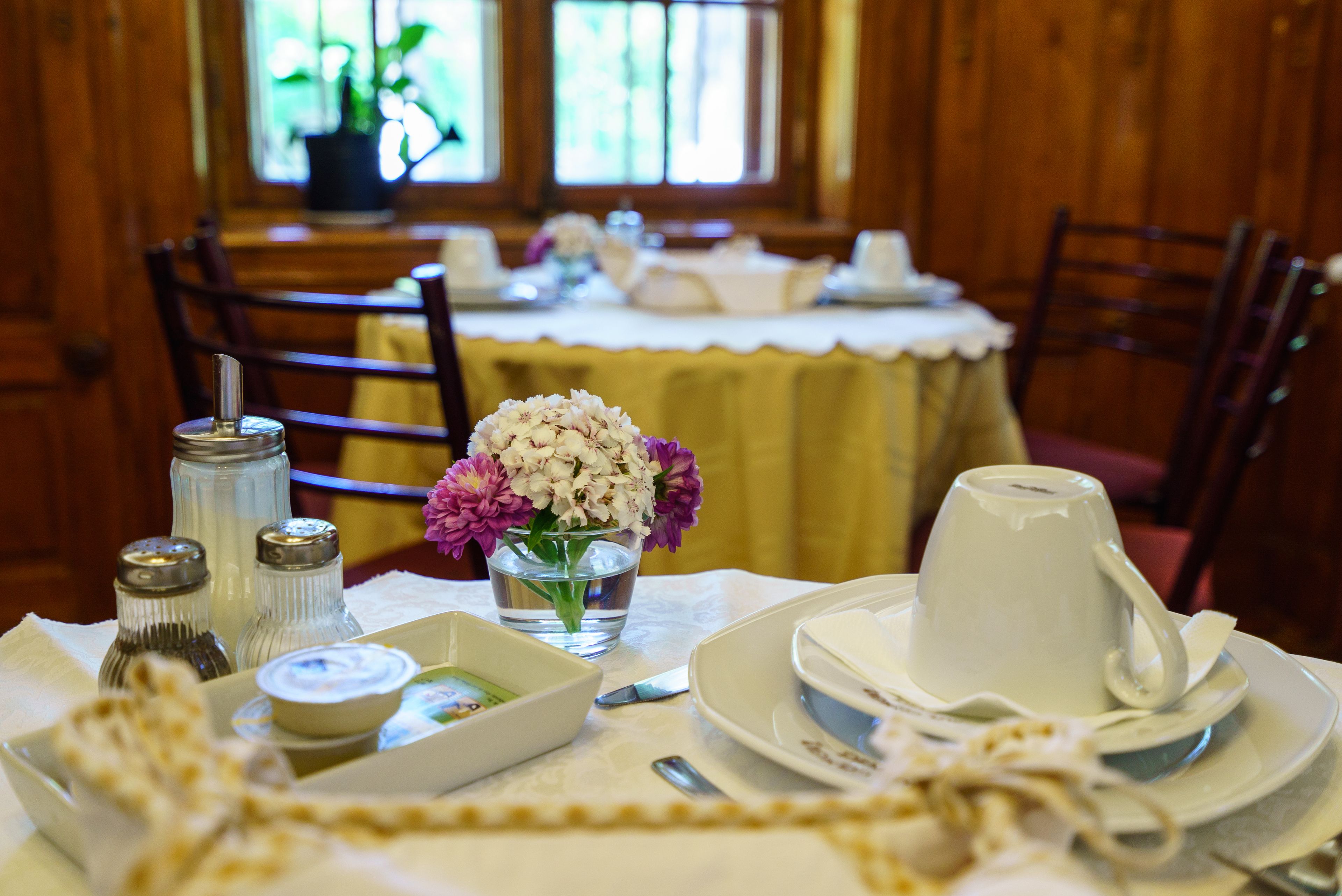 A dining table set with white tableware, a vase of flowers, and condiments.