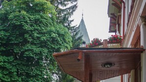 Une cour avec un banc en bois, des pots de fleurs rouges et un bâtiment aux murs blancs et au toit en pente.
