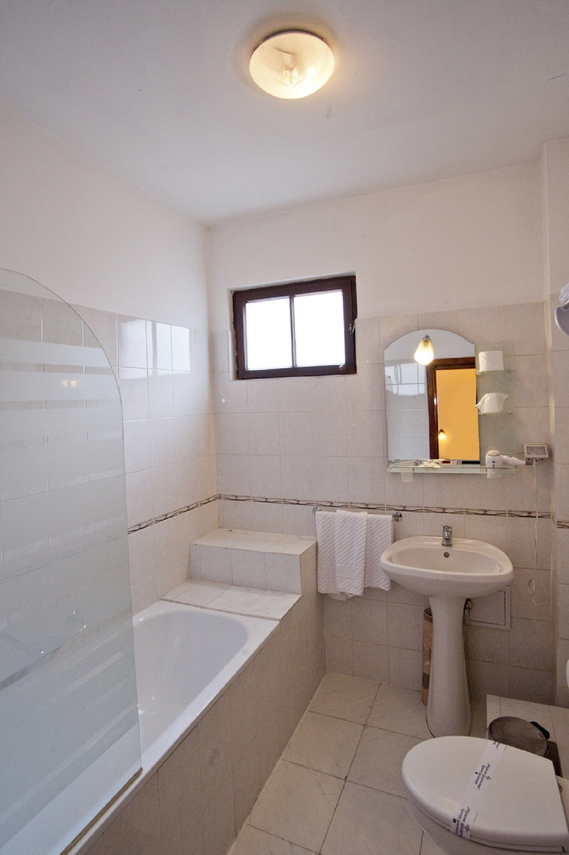 A bathroom with a bathtub, a sink, and a toilet. There is a window above the sink and a mirror on the wall.