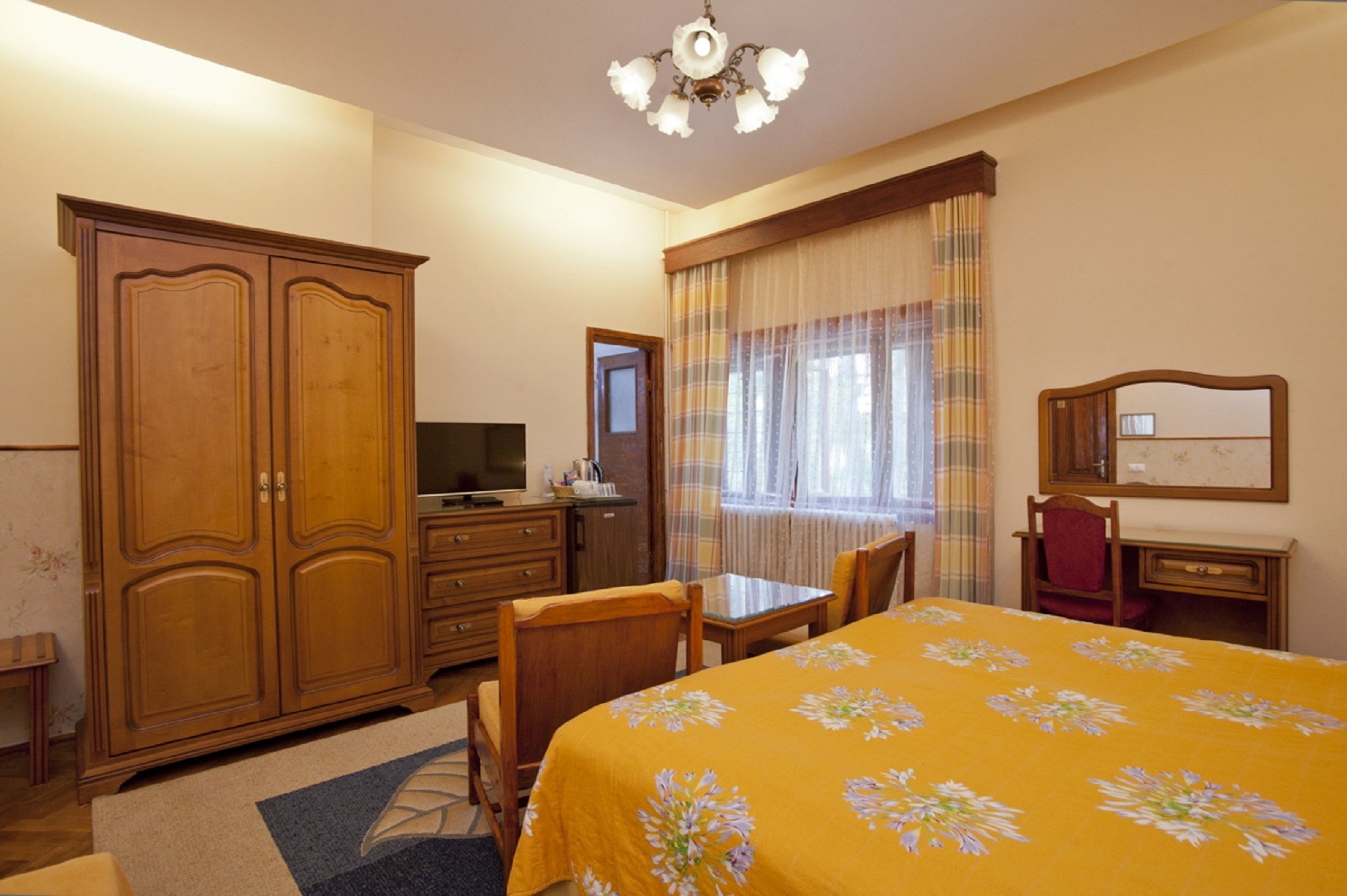 A hotel room with a bed, a desk, a television, a wardrobe, and a window with curtains.