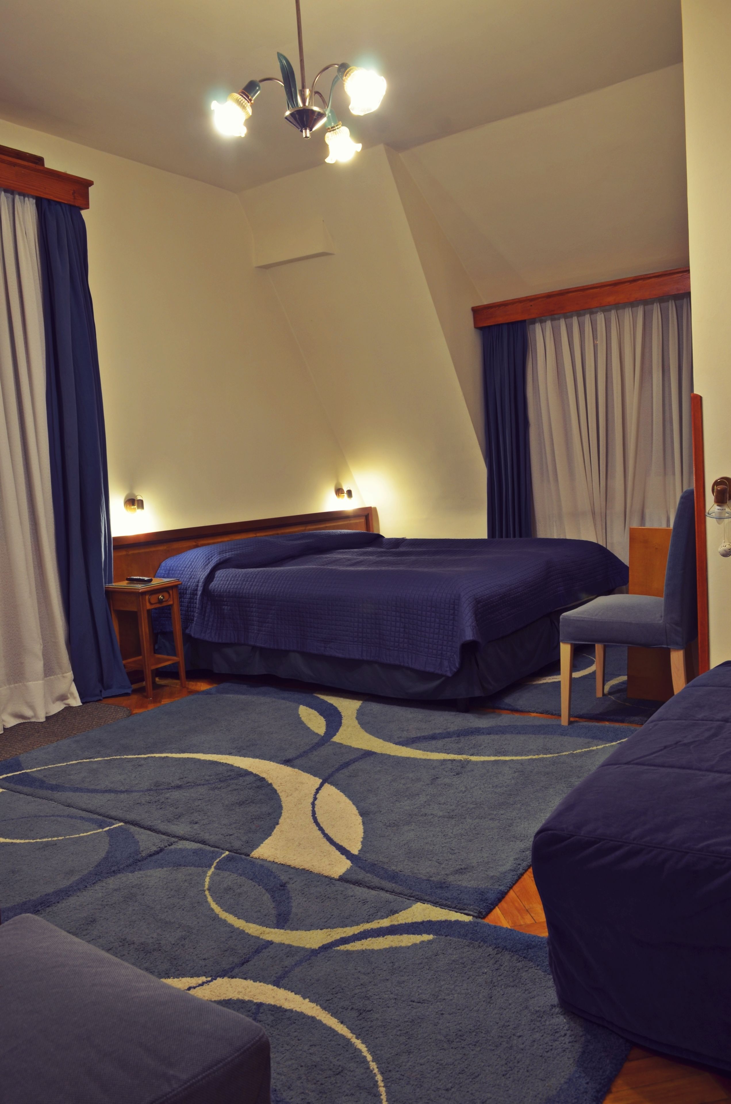 A hotel room with two beds, a desk, a chair, and a large blue patterned rug.