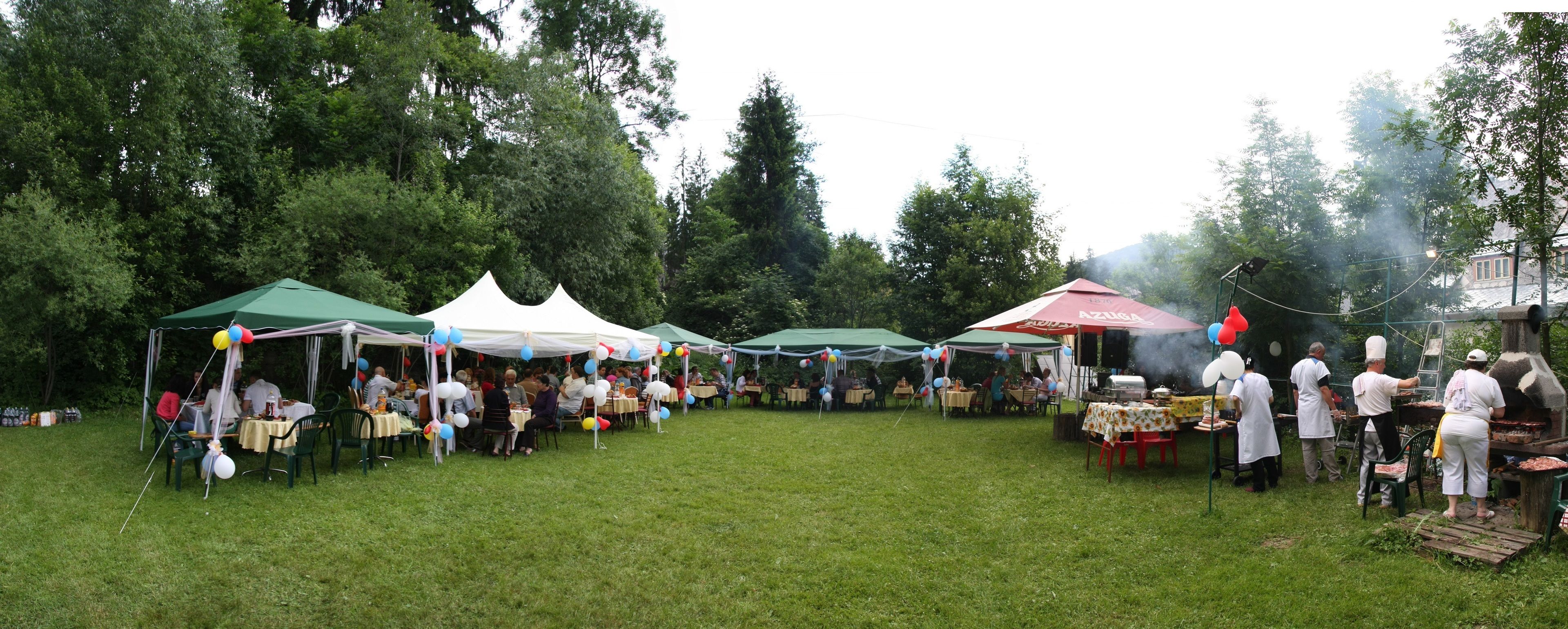 An outdoor event with tents, tables, and people gathered around a barbecue area.