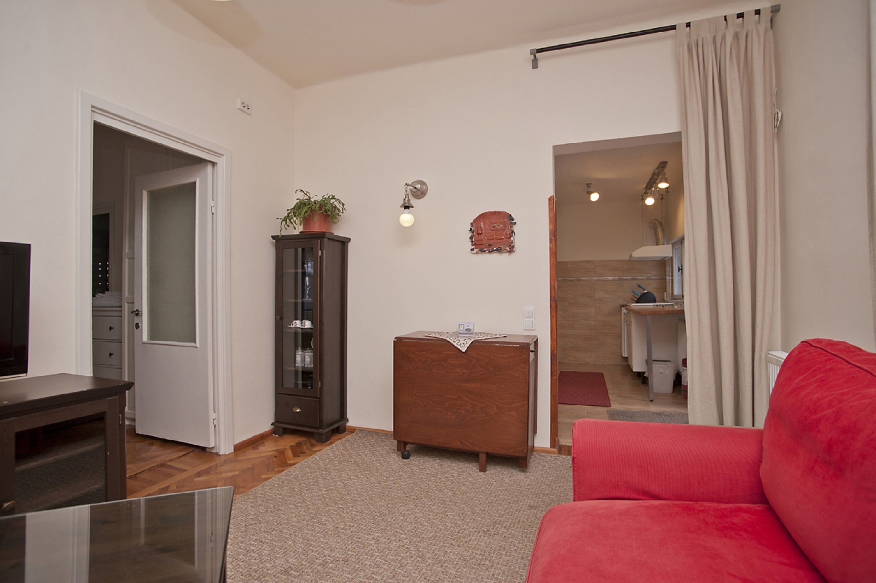 Una sala de estar con un sofá rojo, un armario de madera, un televisor y una puerta que da a un baño.