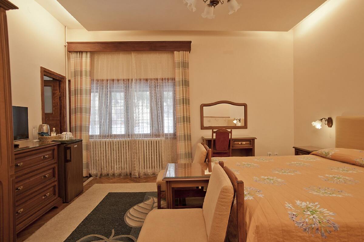 Habitación de hotel con cama, escritorio, silla, cómoda, espejo y ventana con cortinas.